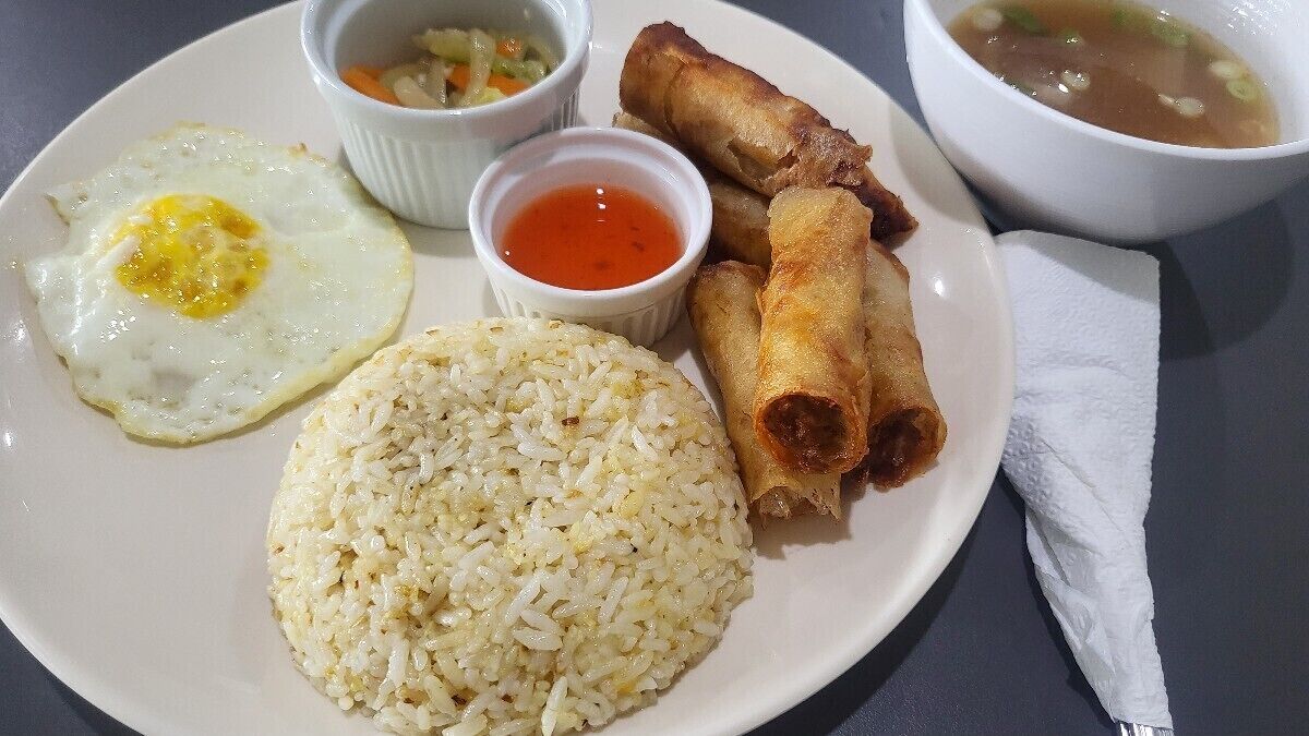 A plate with fried egg, rice, spring rolls, and two small bowls of sauce.