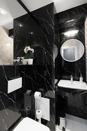 A modern bathroom with black marble walls, a white sink, a mirror, and a toilet. - Vistula - New Exclusive Apartment M11 (Kraków)