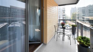 Een balkon met een houten wand, een glazen deur, een tafel met stoelen en planten in potten.