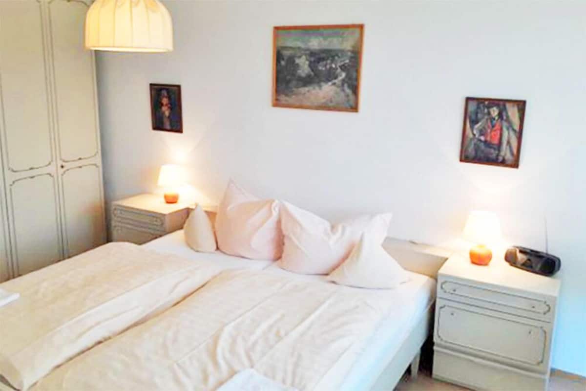 A bedroom with a bed, nightstands, a lamp, and artwork on the wall.