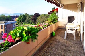 Relax on the balcony with a view of the surrounding neighborhood, surrounded by lush potted plants and a comfortable seating area.