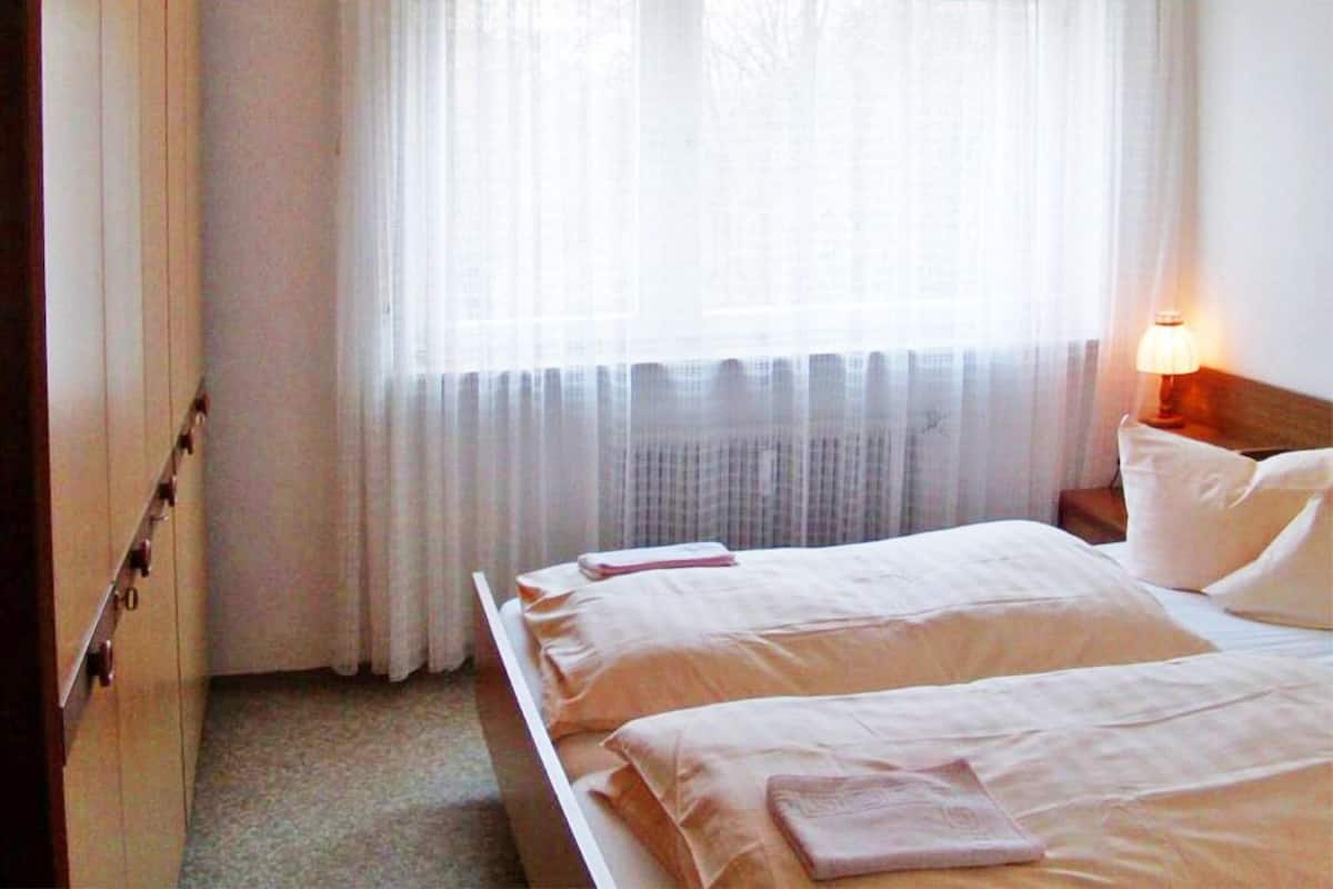 A hotel room with a bed, a nightstand, a lamp, and a window with curtains.