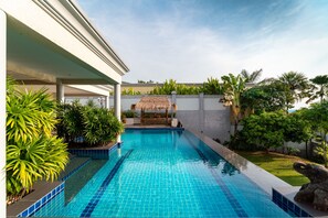 A swimming pool with a thatched roof structure, surrounded by lush greenery and palm trees. - Stunning Luxury Golf and Pool Villas (Pattaya)