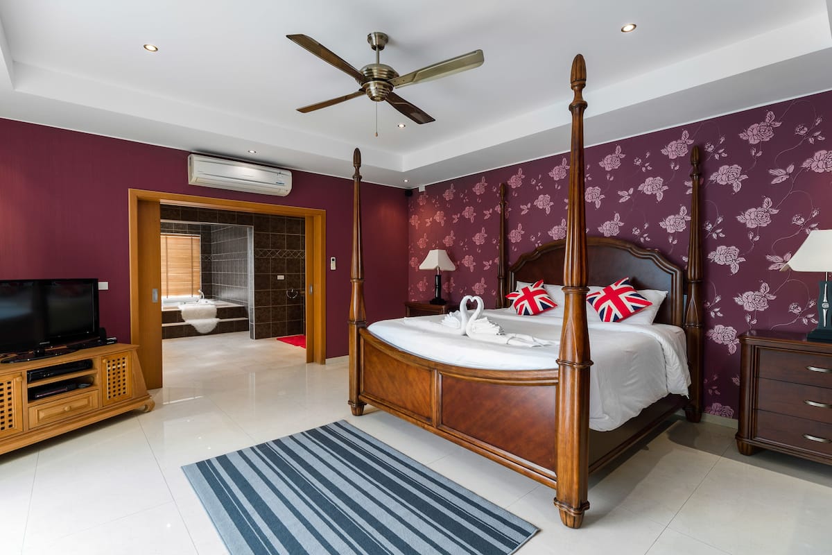 A four-poster bed with a wooden frame, a television on a wooden cabinet, and a bathroom visible through an open door.