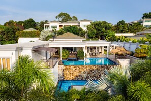 A luxurious pool area with a stone wall, surrounded by lush greenery and modern architecture. - Stunning Luxury Golf and Pool Villas (Pattaya)