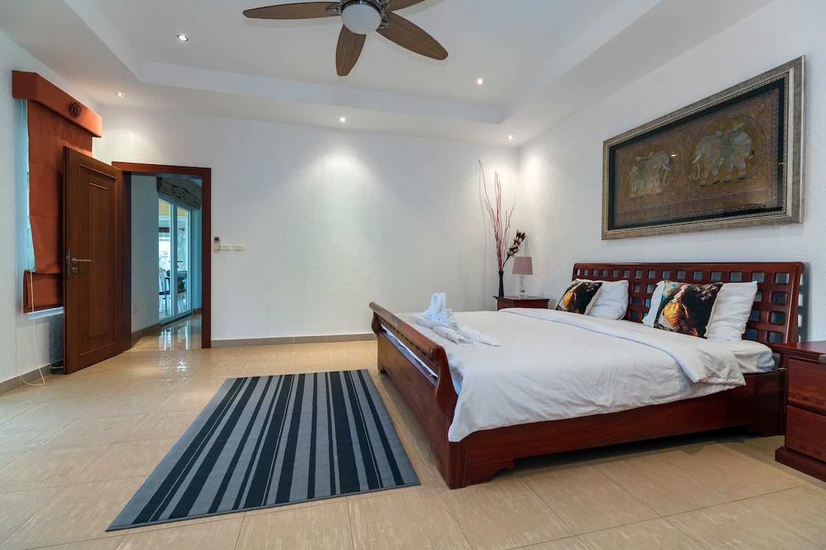 A spacious bedroom with a large bed, a ceiling fan, a wooden headboard, a nightstand, and a framed artwork on the wall.