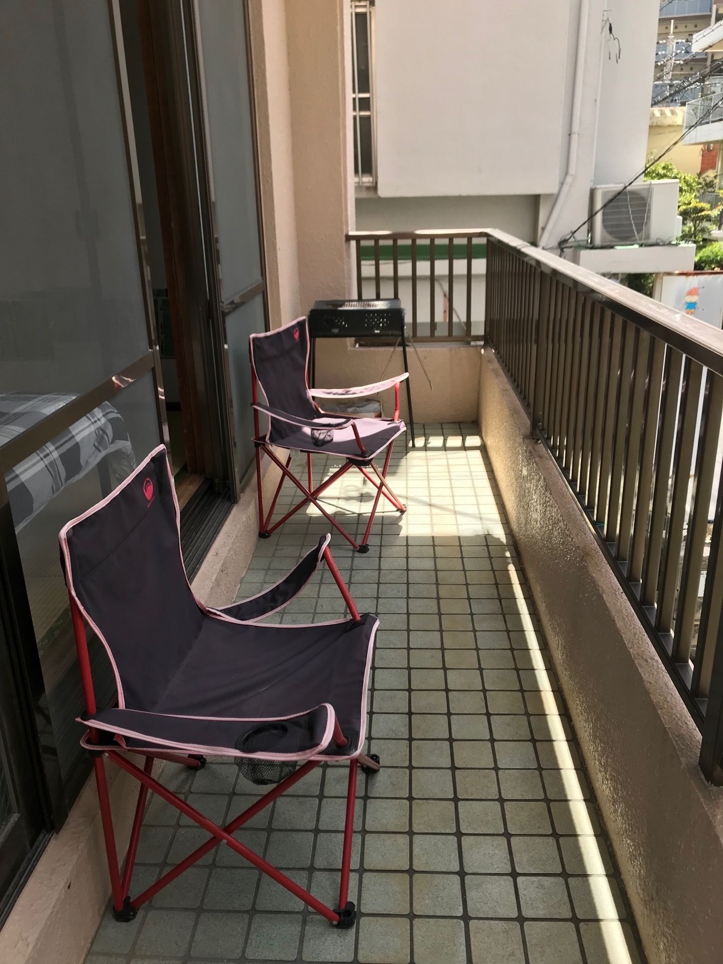 Un balcone con due sedie pieghevoli, un tavolino, pavimento piastrellato e ringhiera in metallo.
