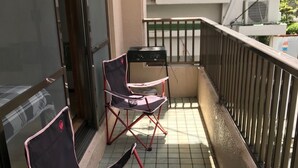 En balkon med to klapstole, et lille bord, flisegulv og gelænder i metal.