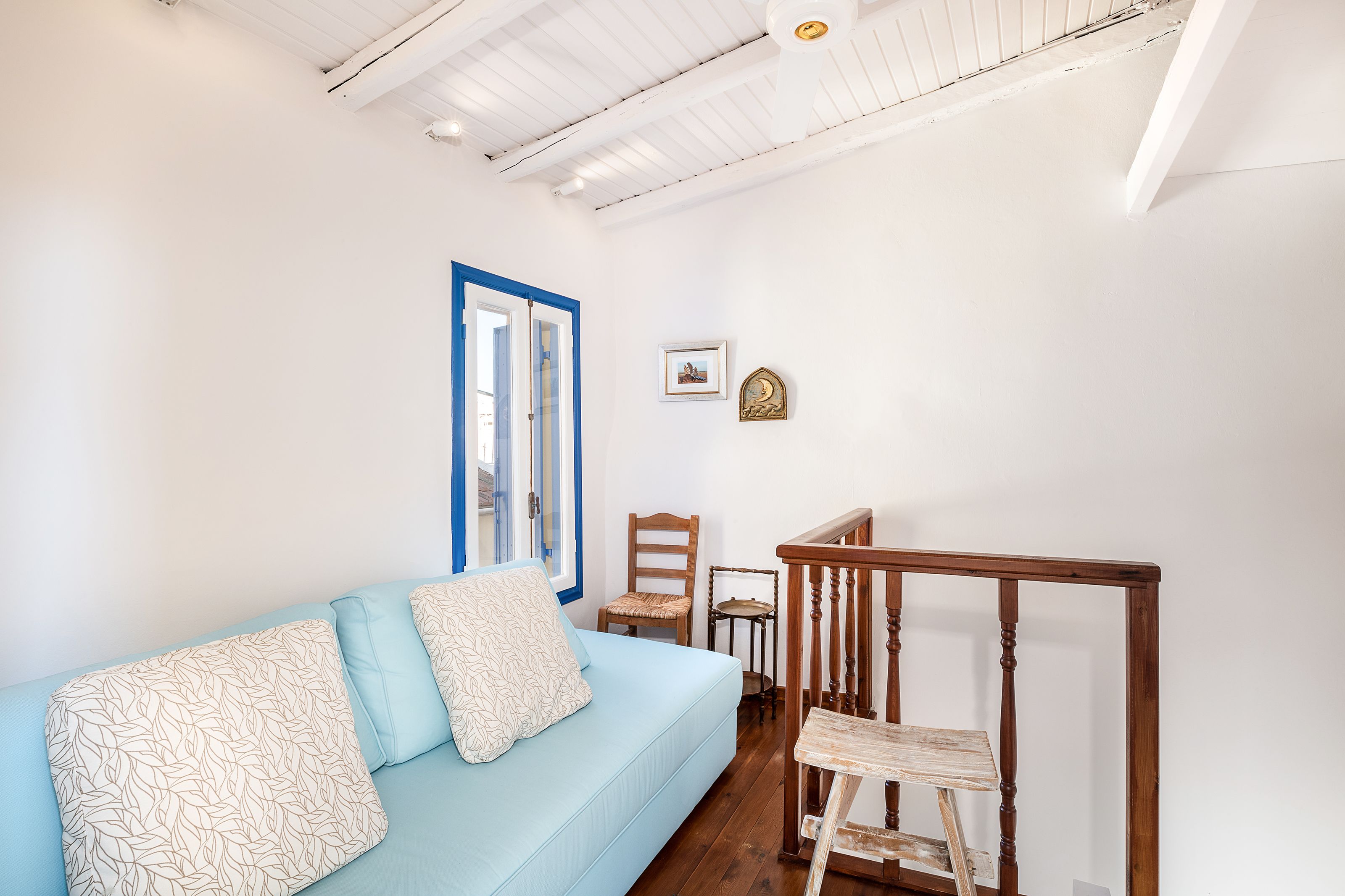 Une pièce avec un canapé bleu clair, une chaise en bois, une petite table et une rambarde en bois.