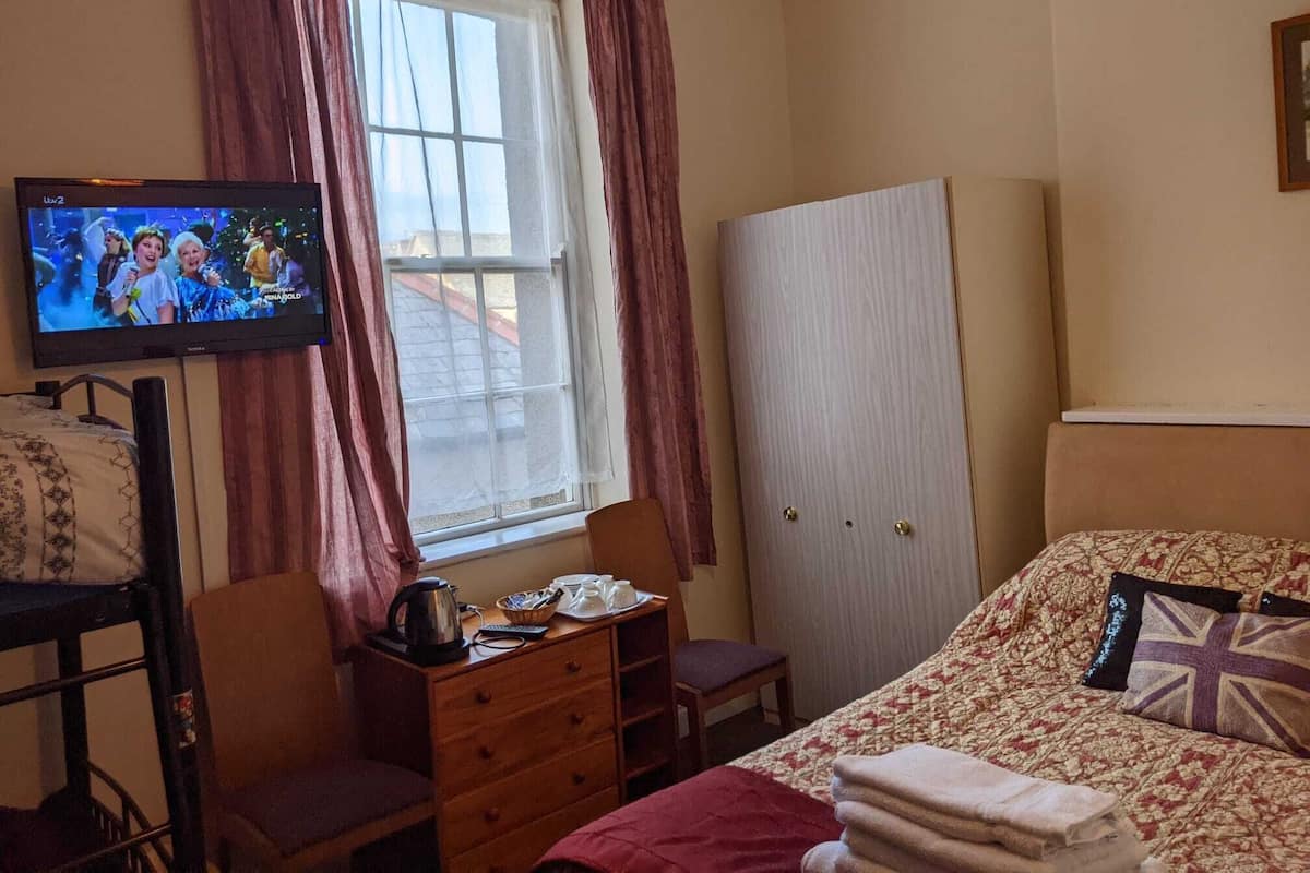 A hotel room with a bed, a desk with a kettle, a television, and a wardrobe.