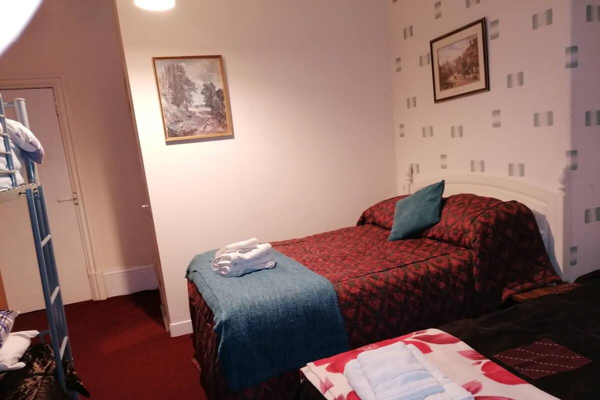 A bedroom with a bed, a blue blanket, and a red bedspread. There are two framed pictures on the wall.