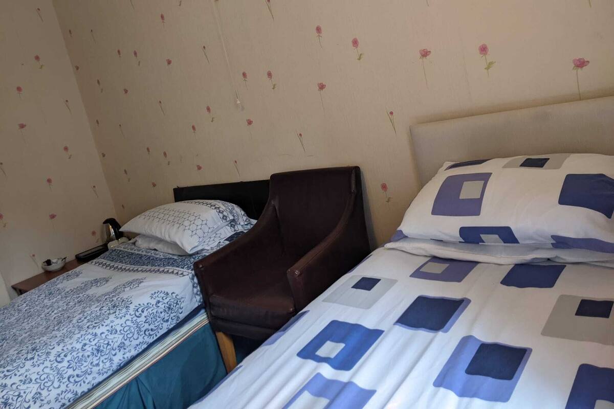 A bedroom with two beds, a chair, and a small table.