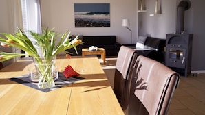 A living room with a wooden table, a sofa, a fireplace, and a painting of a beach scene. - Strandleben Fehmarn - Ferienhaus 3 (Fehmarn)