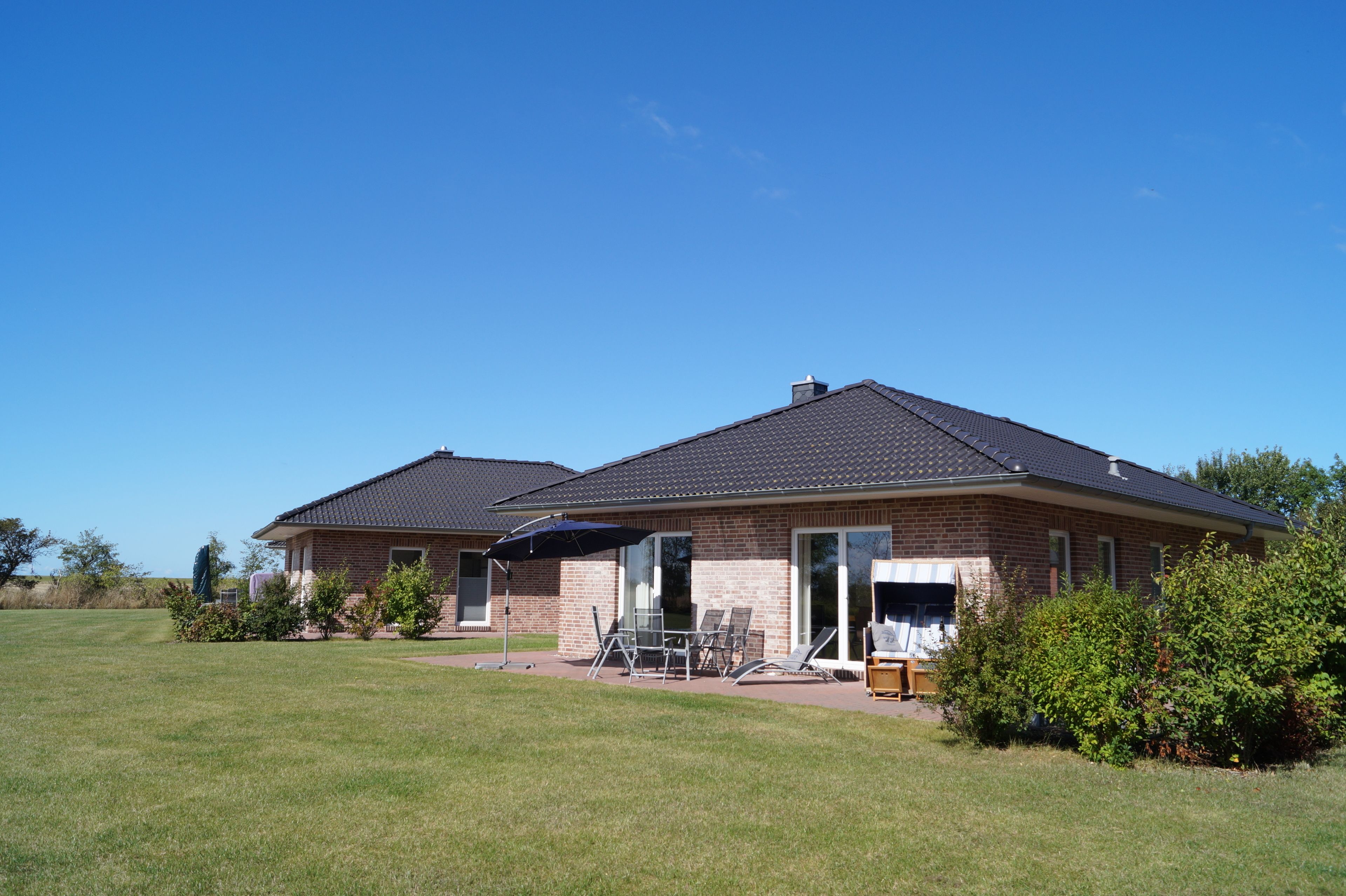 Ein zweigeschossiges Haus mit Backsteinfassade, einer Veranda mit Gartenmöbeln und blauem Himmel.