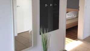 A room with a large mirror, a bed with white bedding, and a small potted plant. - Strandleben Fehmarn - Ferienhaus 3 (Fehmarn)