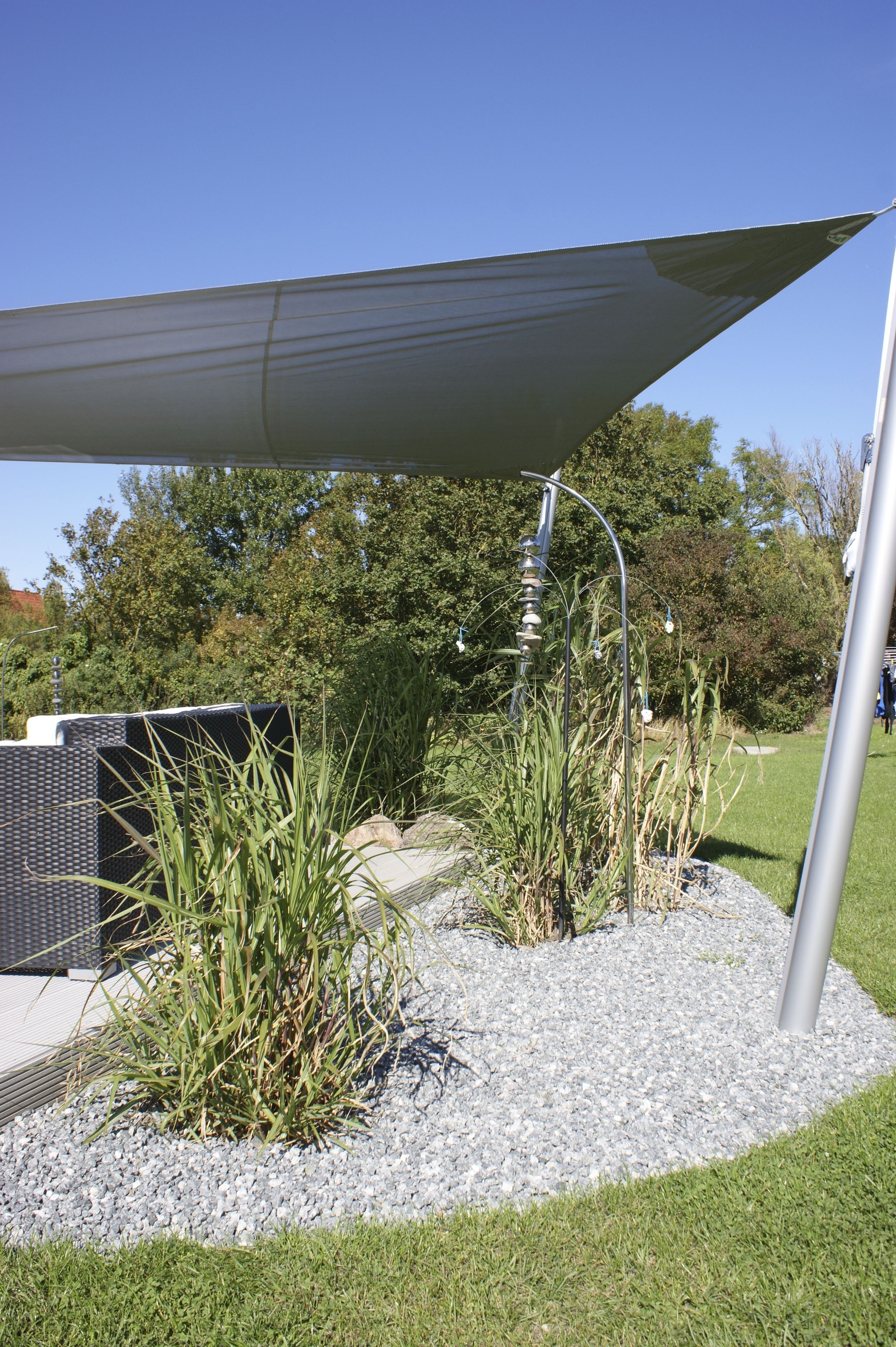 Un espace jardin aménagé avec un coin salon ombragé, une sculpture en métal et un sentier.