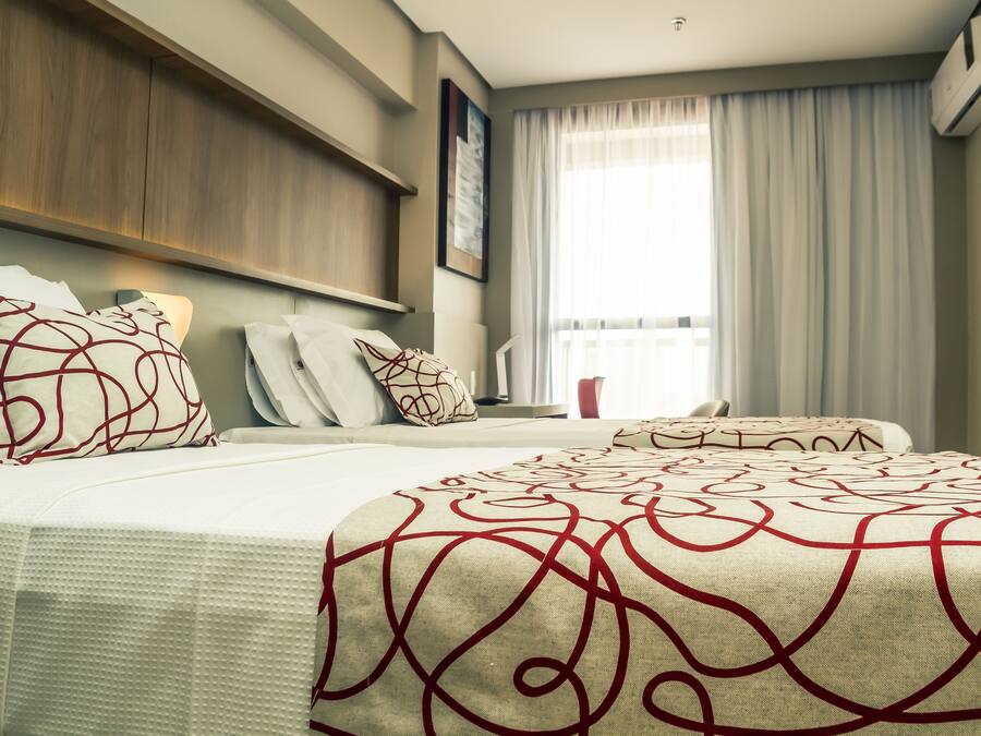 Une chambre d’hôtel avec un grand lit, une table de chevet, une fenêtre avec des rideaux et un climatiseur fixé au mur.