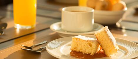 A breakfast setting with a plate of cake, a glass of orange juice, and a cup of coffee on a table.
