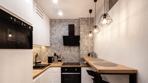 Una cocina compacta con estufa negra, armarios blancos y salpicadero con diseño.