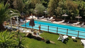 A pool area with lounge chairs and umbrellas, surrounded by lush greenery and hills in the background. - Serraiola Alta (Monterotondo Marittimo)