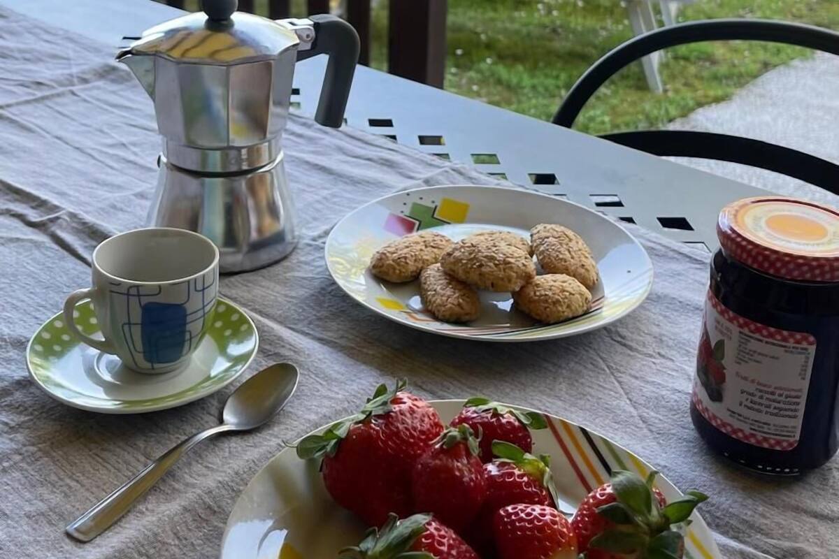 Et bord dækket udendørs med en kaffekande, en tallerken med småkager, en tallerken med jordbær og et syltetøjsglas.