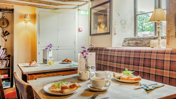 A dining area with a wooden table set for breakfast, a sofa, and a window with a view. - Minnie - Tiger Inn (Eastbourne)