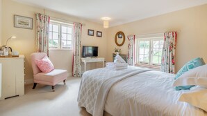 A bedroom with a bed, a chair, a desk with a TV, and two windows with curtains. - Minnie - Tiger Inn (Eastbourne)