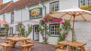A white building with a sign reading "The Tiger Inn" and a brick patio with wooden picnic tables and an umbrella. - Minnie - Tiger Inn (Eastbourne)