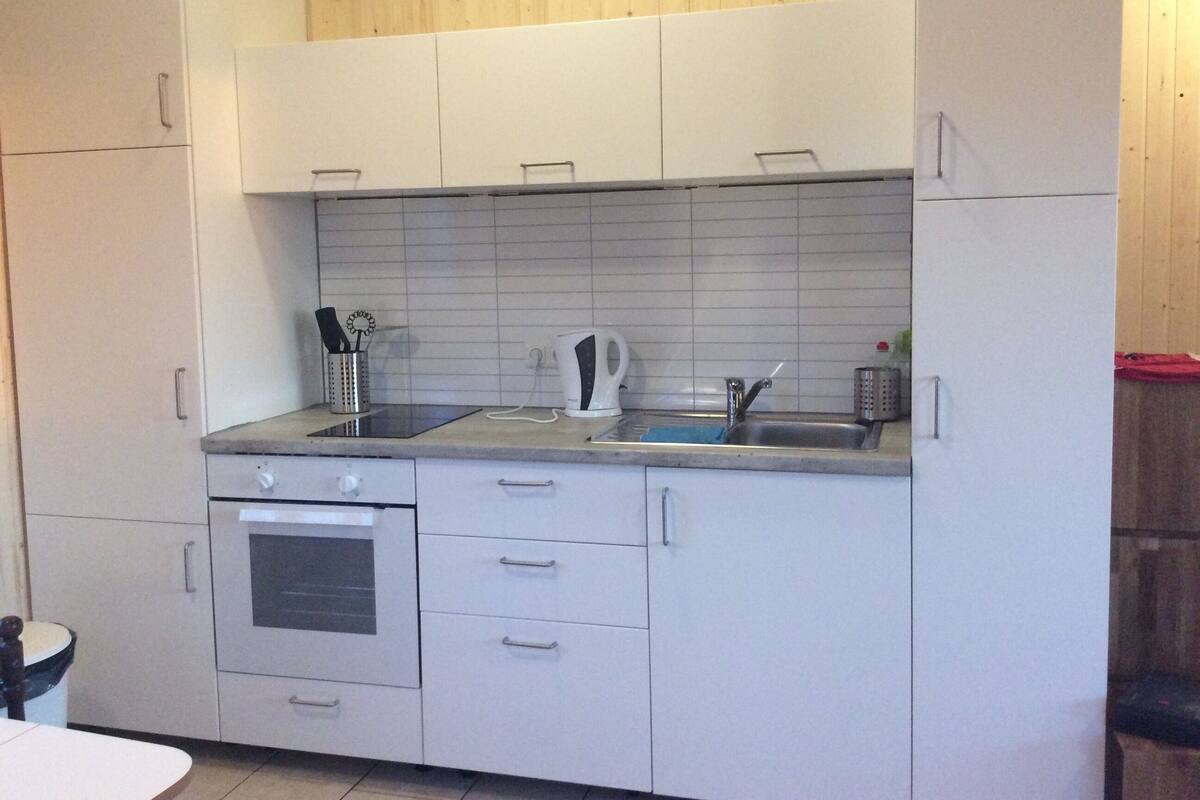 A kitchen with white cabinets, a stainless steel sink, and a kettle.