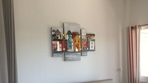 A living room with a beige sofa, a coffee table, and a wall-mounted artwork depicting colorful houses.