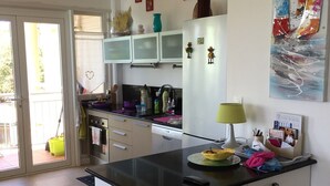 A modern kitchen with a central island, white cabinetry, a microwave, and a refrigerator. There is a window with a view of the outdoors, and a painting on the wall.