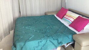 A bed with a teal quilt, a beige headboard, and a colorful striped pillow.