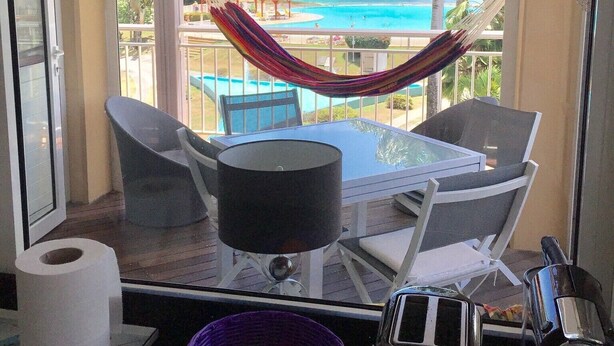 A balcony with a view of the ocean, a hammock, and a table with chairs.