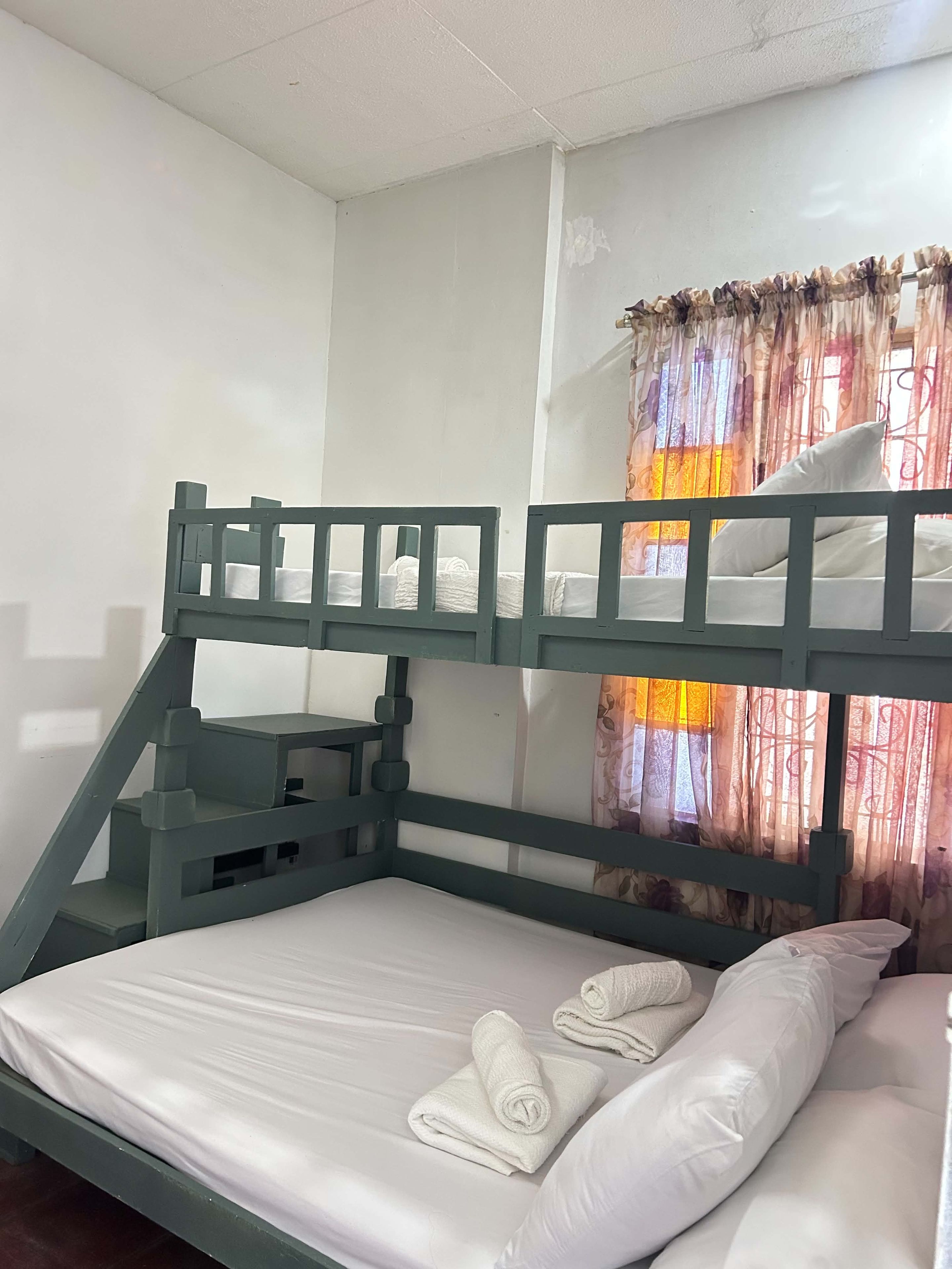 Een stapelbed met een houten frame, een matras, kussens en opgerolde handdoeken.