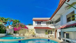 Une piscine à l’eau d’un bleu limpide, entourée d’un bâtiment blanc doté d’un toit rouge et de balcons.