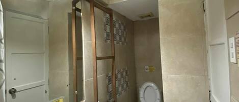 Ein Badezimmer mit Waschbecken, Spiegel und Toilette. Ein Schild ist an der Wand angebracht, und es gibt eine Tür mit Griff.