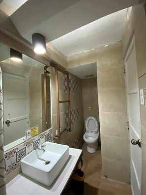 A bathroom with a white sink, a mirror, and a toilet. There is a notice on the wall and a door with a handle. - The Palacio de Laoag (Laoag)