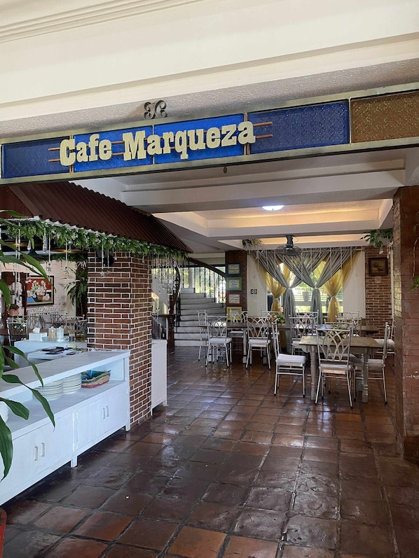 Un café llamado Cafe Marquez con un interior rústico, que presenta paredes de ladrillo, pisos de baldosas y diversos arreglos de asientos.