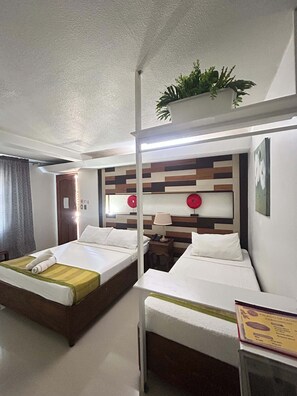 A hotel room with two beds, a bedside table with a lamp, a small table with a menu, and a potted plant on the wall. - The Palacio de Laoag (Laoag)