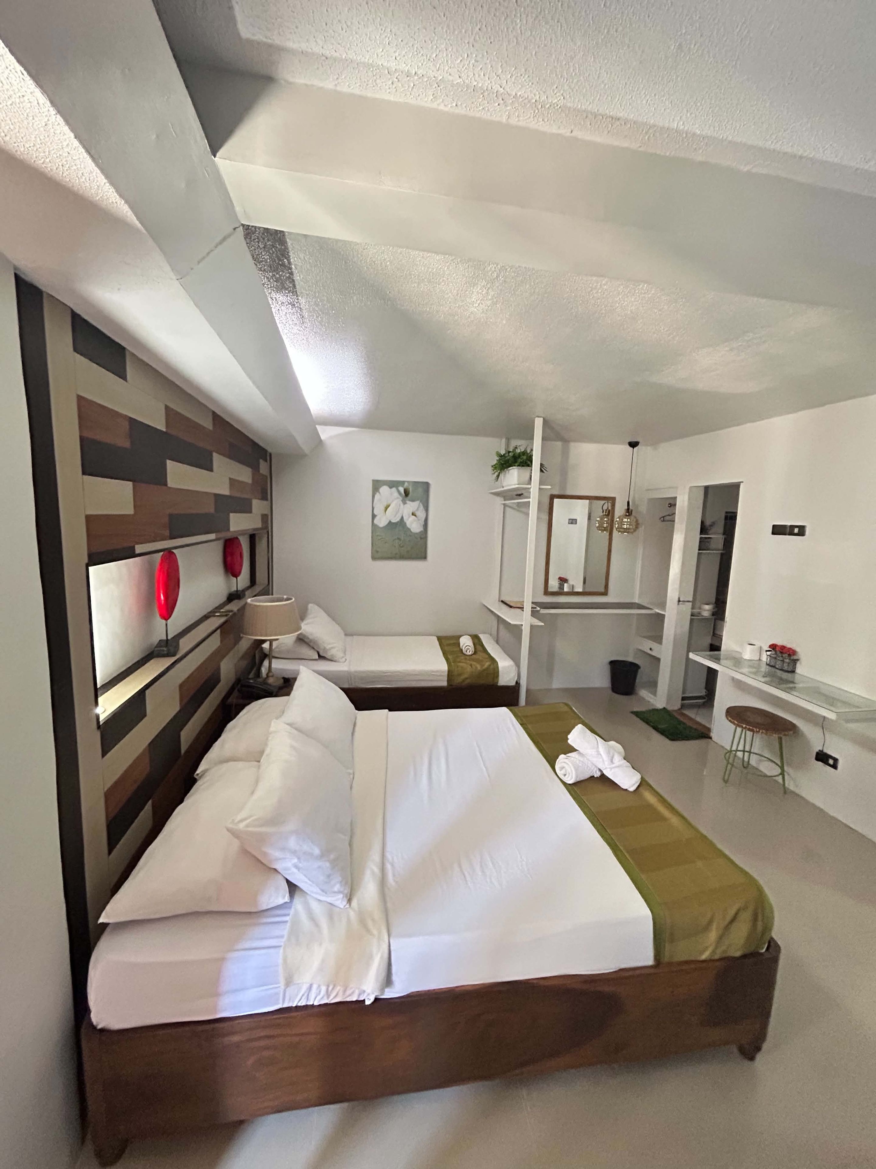 A hotel room with two beds, a desk, a mirror, and a small seating area.