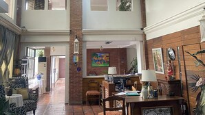 Un hall d’entrée spacieux avec un plafond haut, un lustre, un comptoir de réception et un coin salon agrémenté de canapés à motifs.