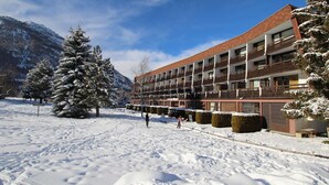 Un hôtel à plusieurs étages, doté de balcons, entouré d’arbres et de montagnes enneigées.