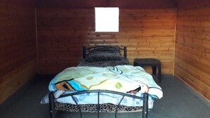 A small, cozy room with wooden walls and a sloped ceiling. It features a single bed with a patterned blanket and a small bedside table. - Desert Lovers Camp (Wadi Rum)