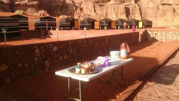 A dining table with food and drinks in a desert setting with rock formations in the background. - Desert Lovers Camp (Wadi Rum)