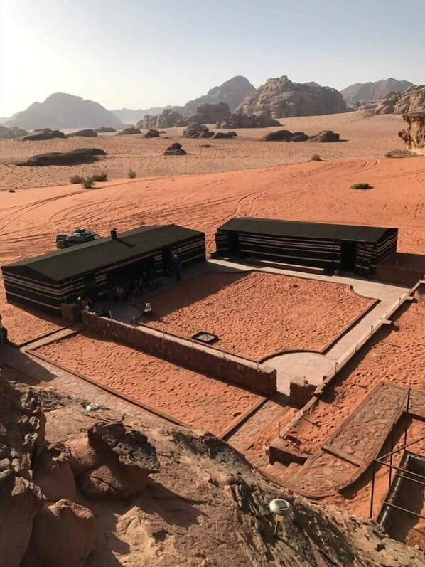 A desert landscape with two large, modern buildings with flat roofs, surrounded by a paved area and a sandy path. - Desert Lovers Camp (Wadi Rum)