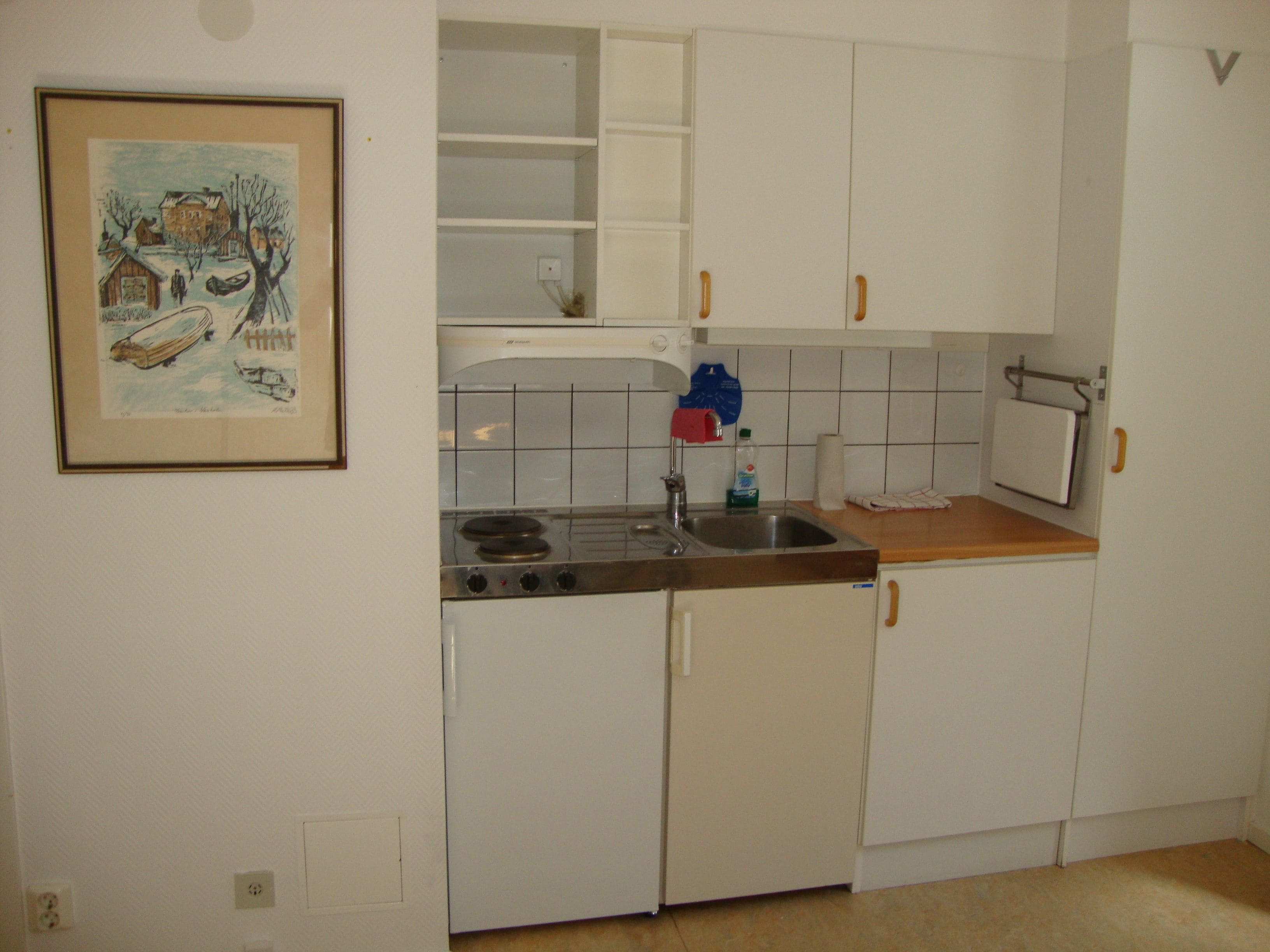 A kitchen with white cabinets, a stove, and a sink. There is a framed picture on the wall.