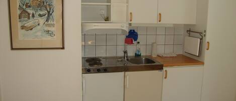 A kitchen with white cabinets, a stove, and a sink. There is a framed picture on the wall.