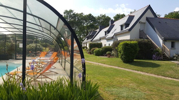 A conservatory with a glass ceiling, a swimming pool, and a well-maintained lawn with a house in the background.