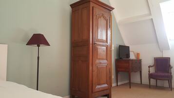Ein Zimmer mit einem hohen Holzschrank, einem Schreibtisch mit Computer, einem Stuhl und einer Stehlampe.