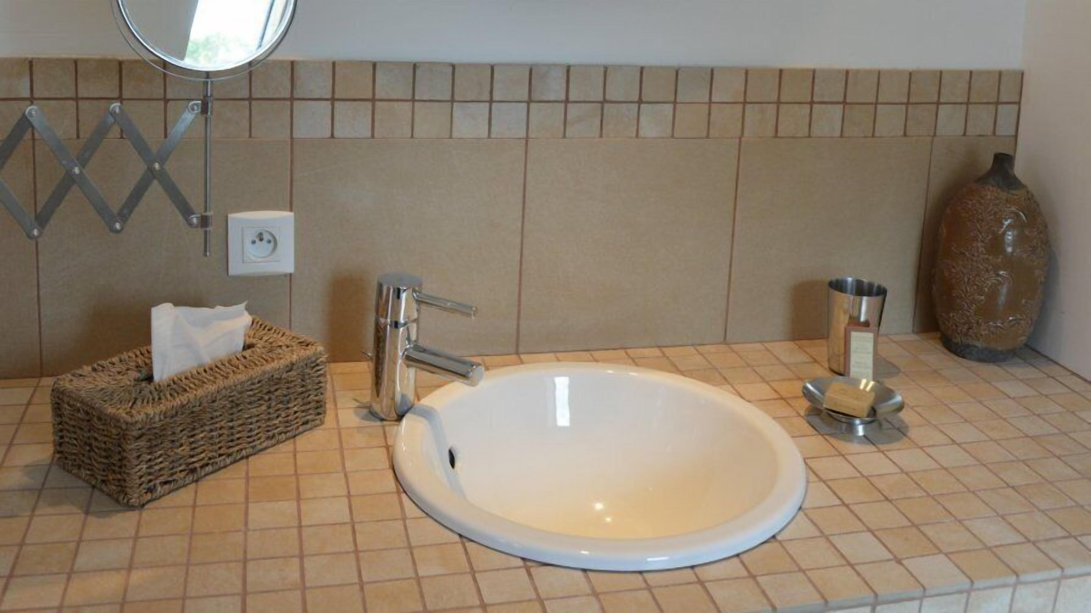 Ein Badezimmer mit einem weißen Waschbecken, einem chromfarbenen Wasserhahn und einer kleinen Vase.
